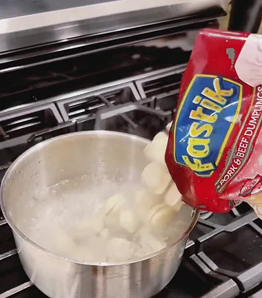 A Fastik Pork and Beef Dumplings bag being tipped into a boiling saucepan on a gas hob
